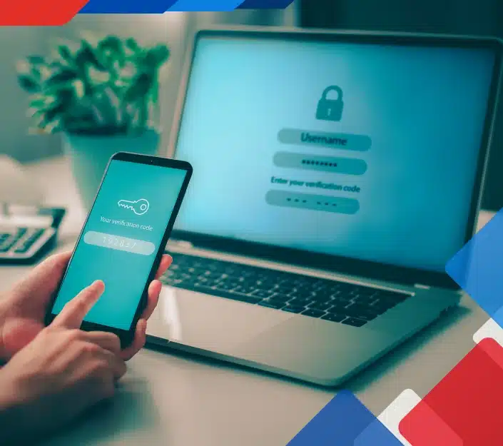A person holds a smartphone showing a verification code, with a laptop in the background displaying a login screen. Concept of secure authentication.